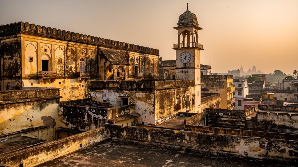 Weathered palace ramparts and a clock tower rising above flat rooftops in Dhrangadhra