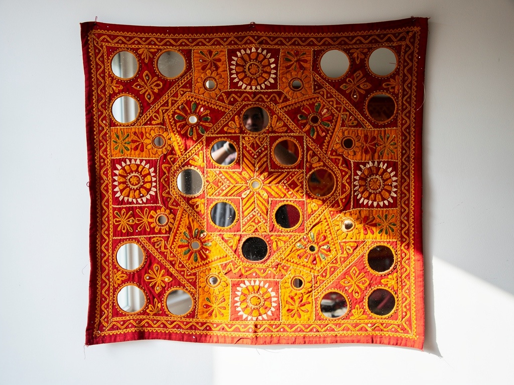 Gujarati mirror-work applique textile in red, orange and yellow hung on a white wall