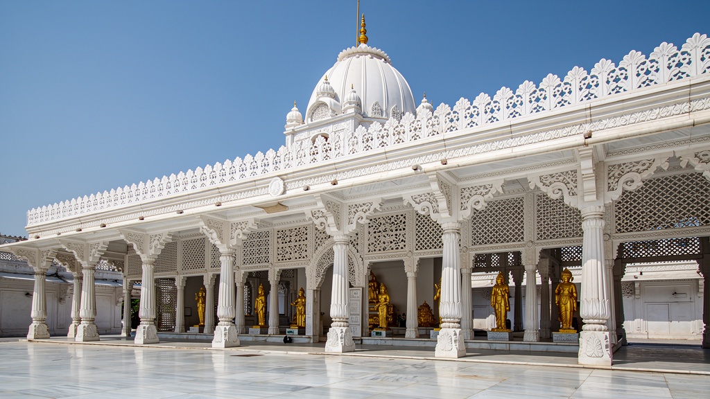 White marble Jain Trimandir temple complex with a long colonnade under bright light